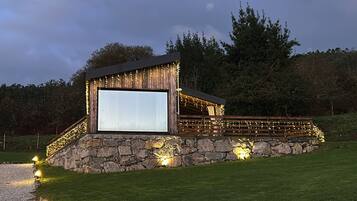 Ein rustikales Freiluftkino mit großer Leinwand, Steinwänden und Lichterketten.