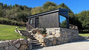 A modern wooden cabin with a stone base, large windows, and a staircase leading to the entrance.