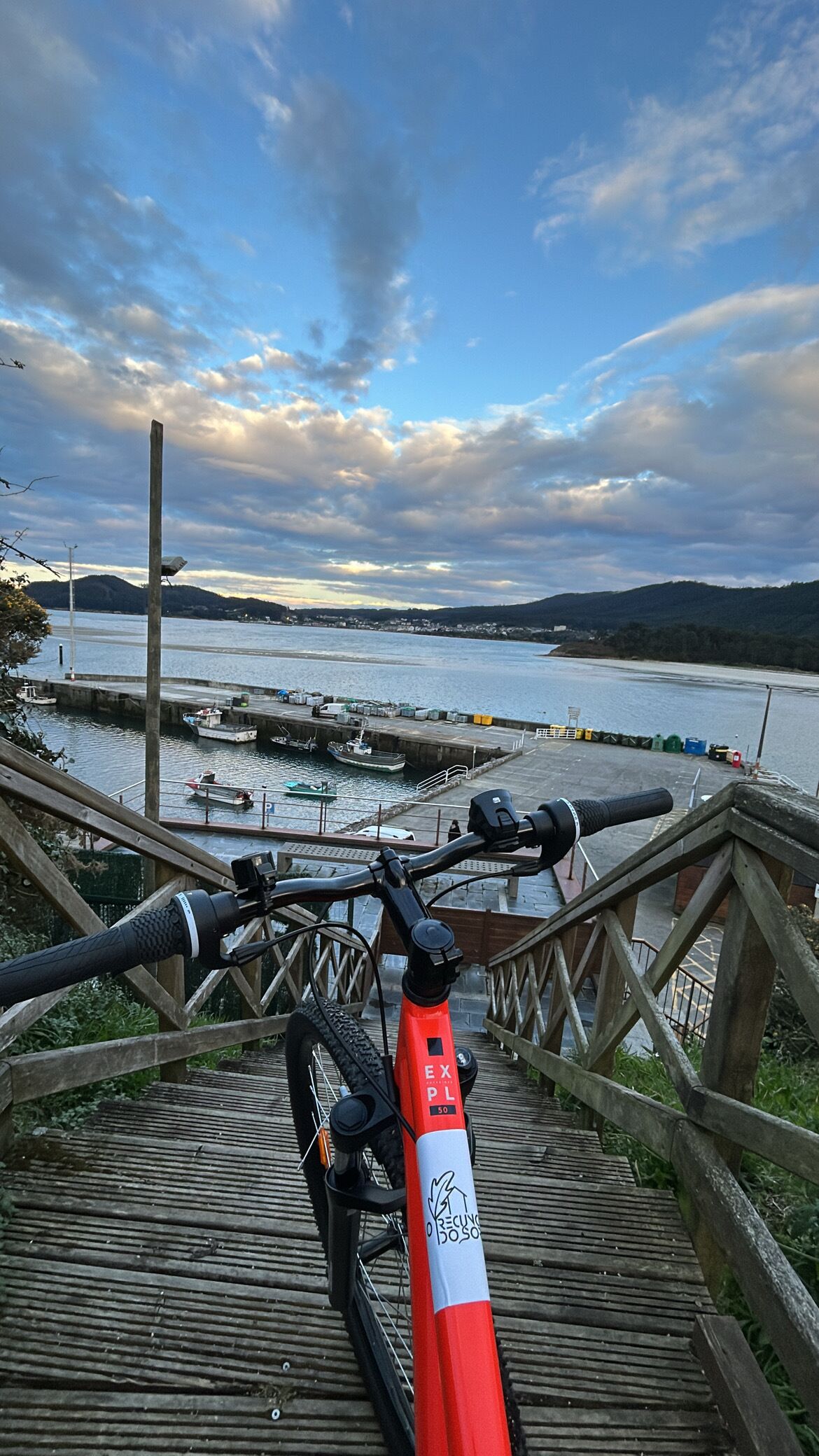A bicycle parked on a wooden staircase overlooking a harbor with boats and a cloudy sky.