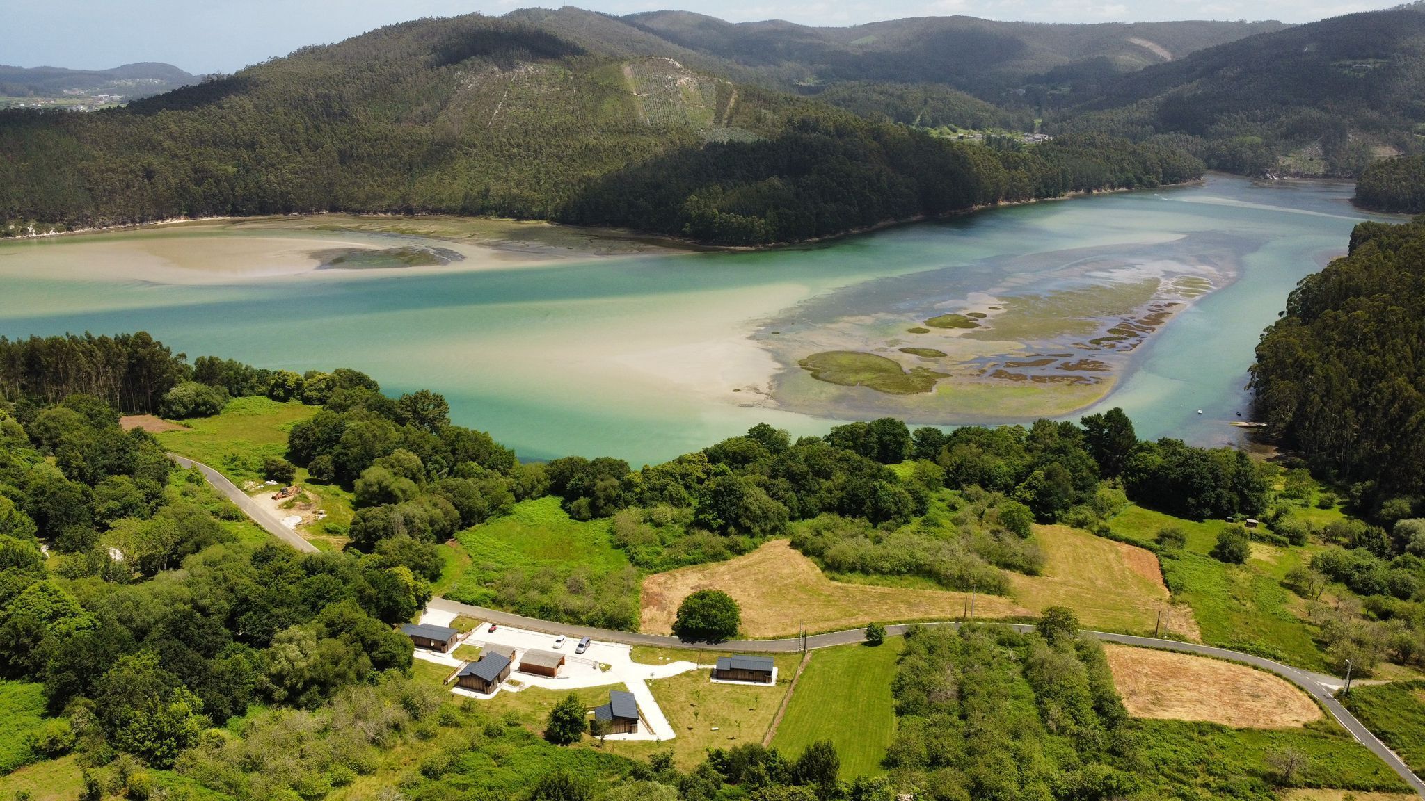 An aerial view of a coastal area with a small cluster of buildings surrounded by lush greenery and a large body of water.