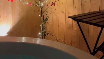 A wooden cabin interior with a hot tub and a decorative plant with red flowers and lights.
