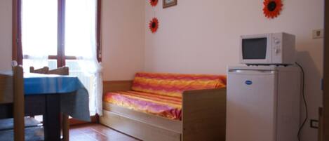 Una habitación pequeña con cama, una mesita y un refrigerador.