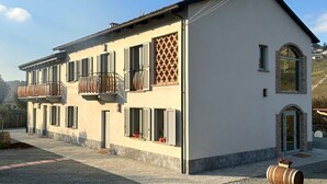 A two-story building with a balcony, a small entrance with a door, and a gravel driveway.