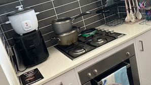A kitchen with a gas stove, a slow cooker, a coffee maker, and a kettle. There are cabinets, a microwave, and a towel hanging on the oven door.