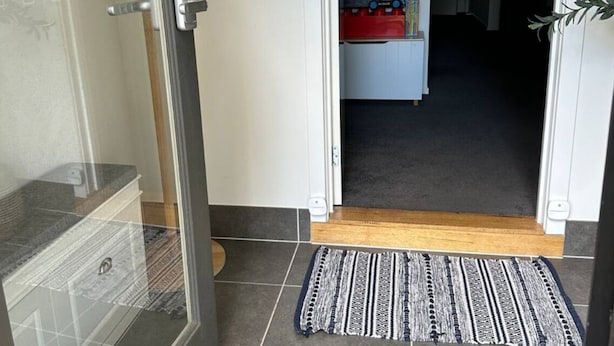 A doorway leading to a room with a tiled floor, a wooden door, and a small rug.