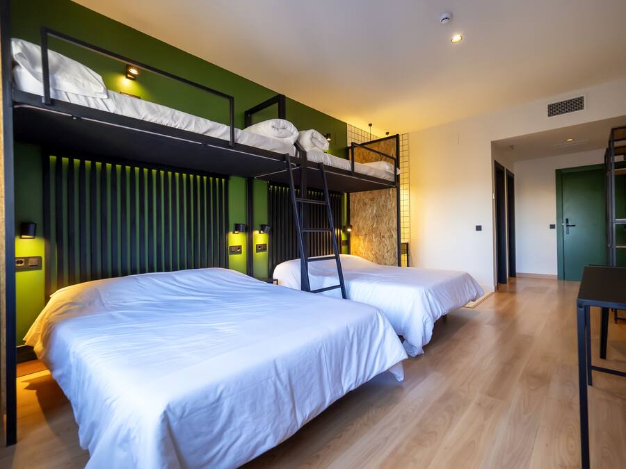 Una moderna camera d'albergo con due letti singoli, un letto a castello, pavimento in legno e pareti verdi.