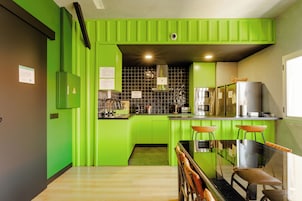 A modern kitchen with green cabinetry, a black countertop, and a wooden dining table with stools.