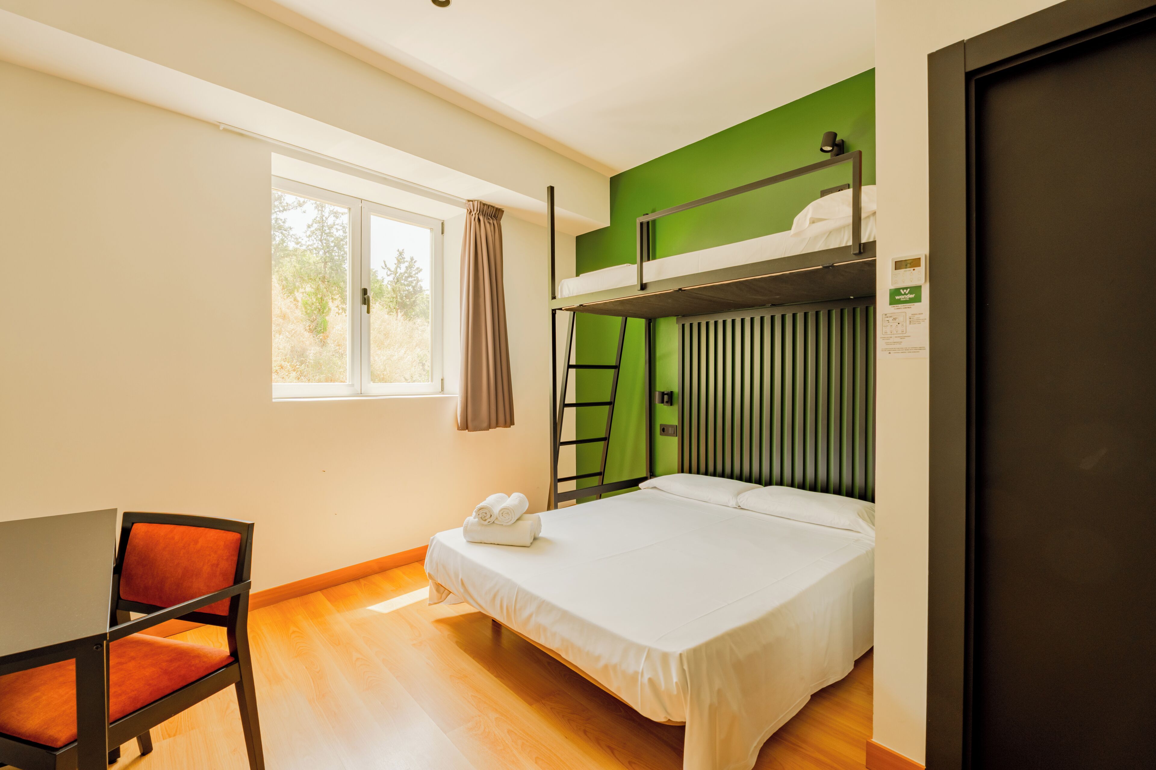 Une chambre avec un lit superposé, un bureau avec une chaise, une fenêtre avec des rideaux et une porte.