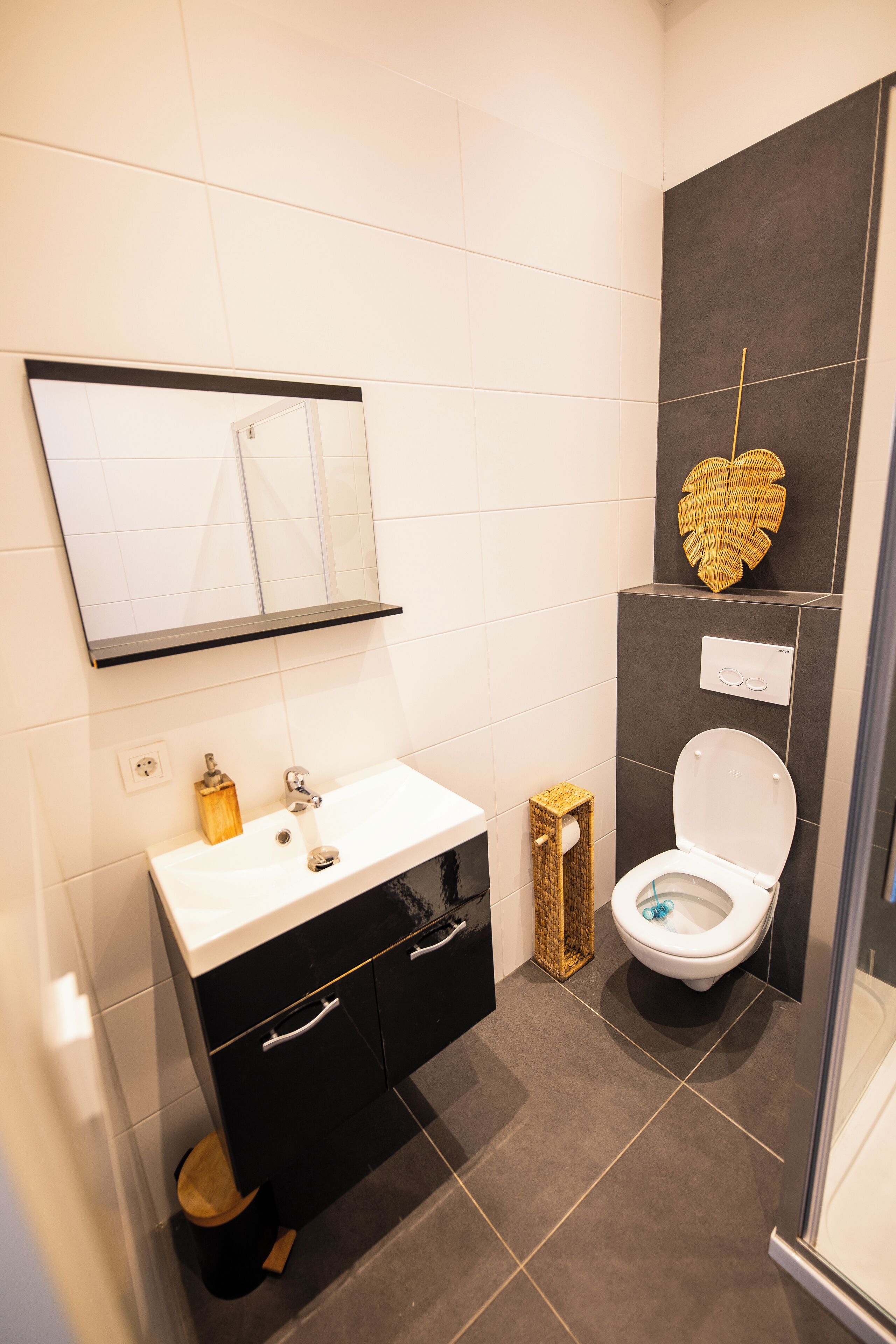 A modern bathroom with a white sink, black cabinets, a mirror, a toilet, and a shower area.