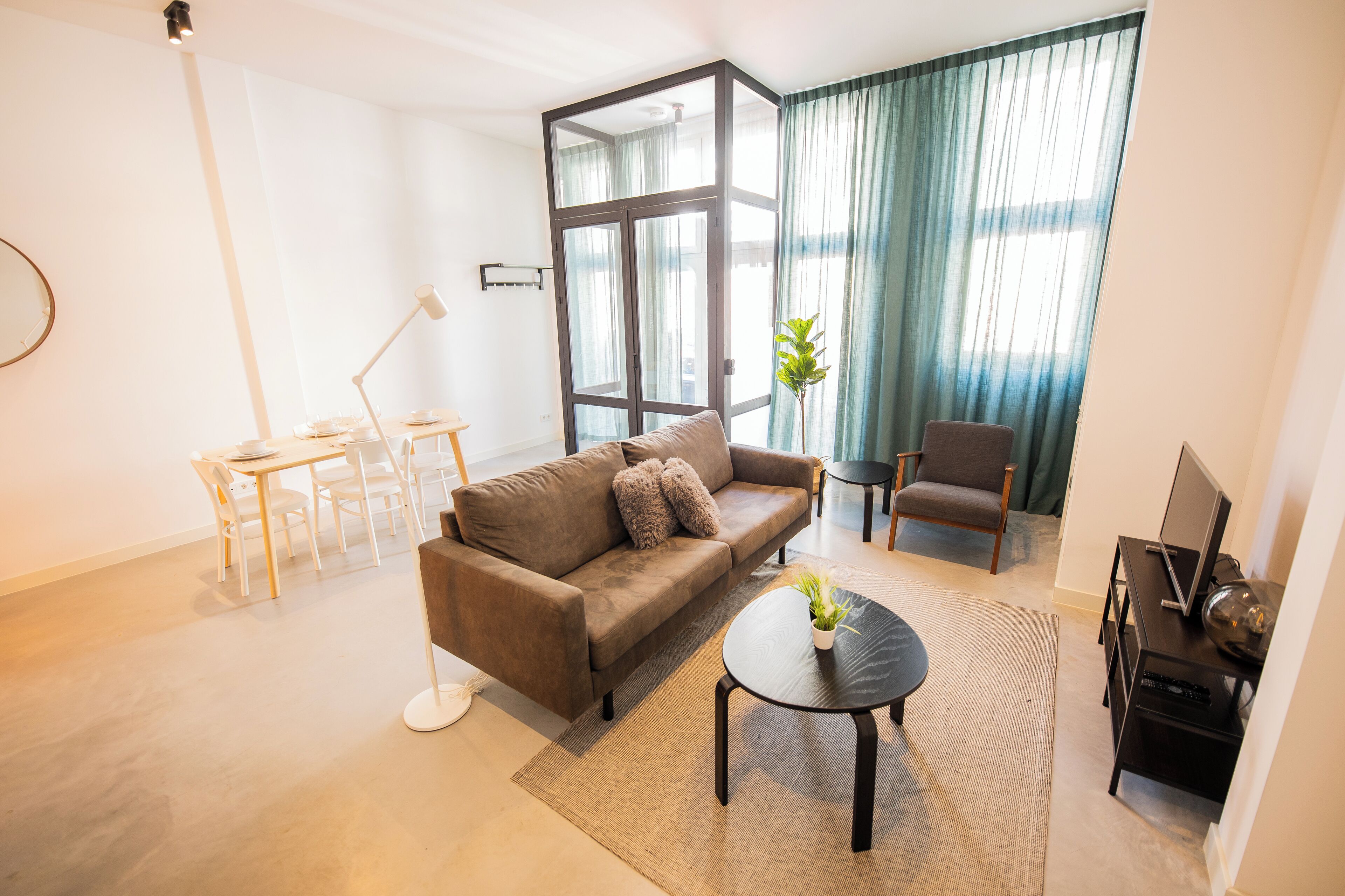 A modern living room with a brown sofa, a round coffee table, a TV stand, and a dining area with a white table and chairs.