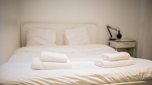 A neatly made bed with white linens and two folded towels on the bed.