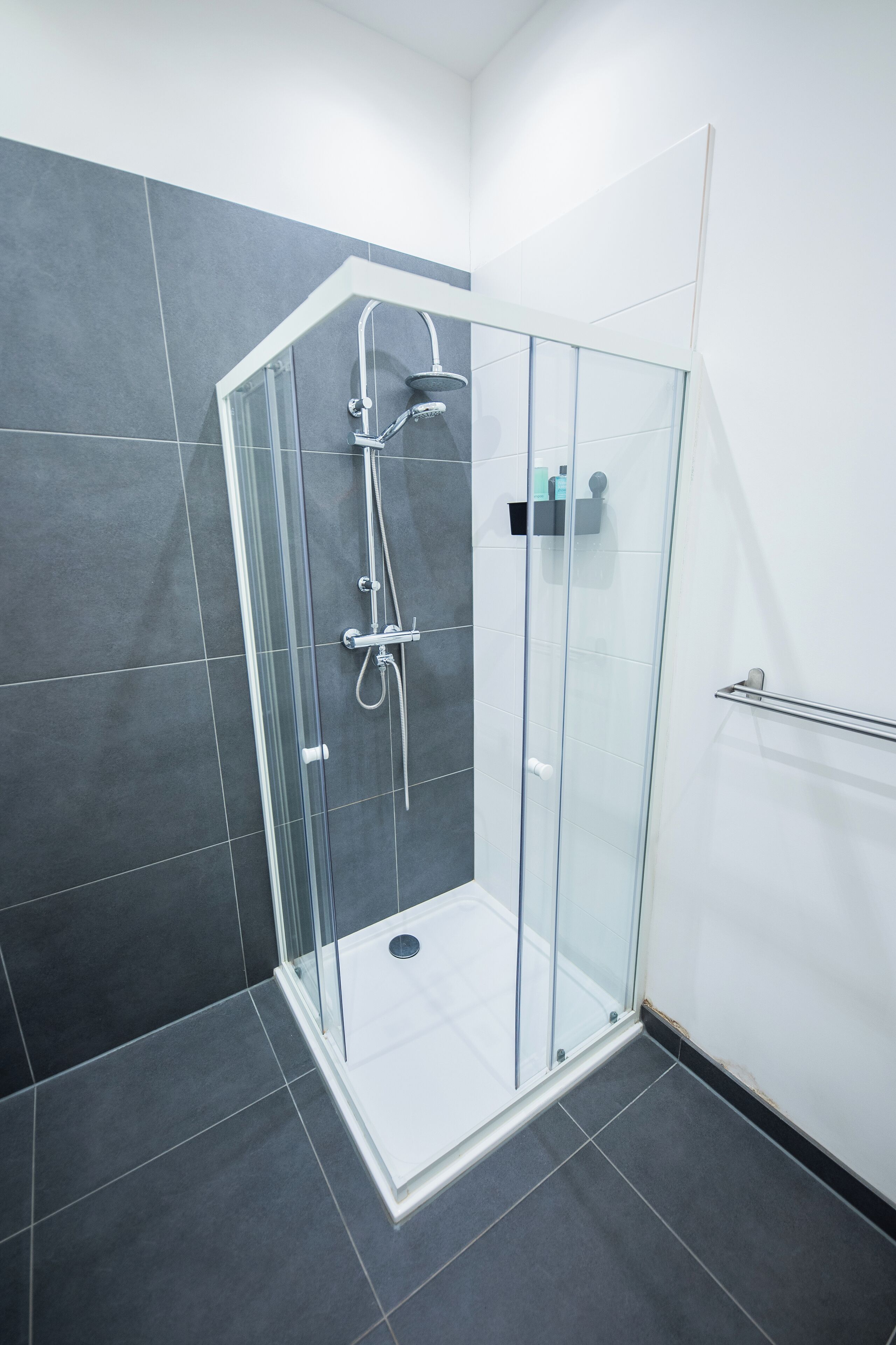 A glass-enclosed shower stall with a white base and a grey tiled wall.