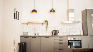 A modern kitchen with grey cabinets, a stainless steel range hood, a built-in oven, and pendant lighting.