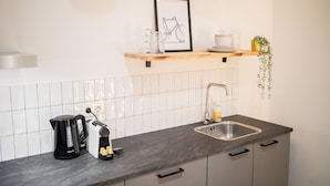 A modern kitchen with a black coffee maker, a toaster, and a sink. There is a framed bicycle picture on the wall and a small plant on the counter.