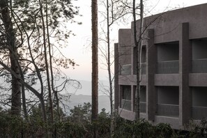 Un edificio moderno con varios balcones, rodeado de árboles y un paisaje montañoso.