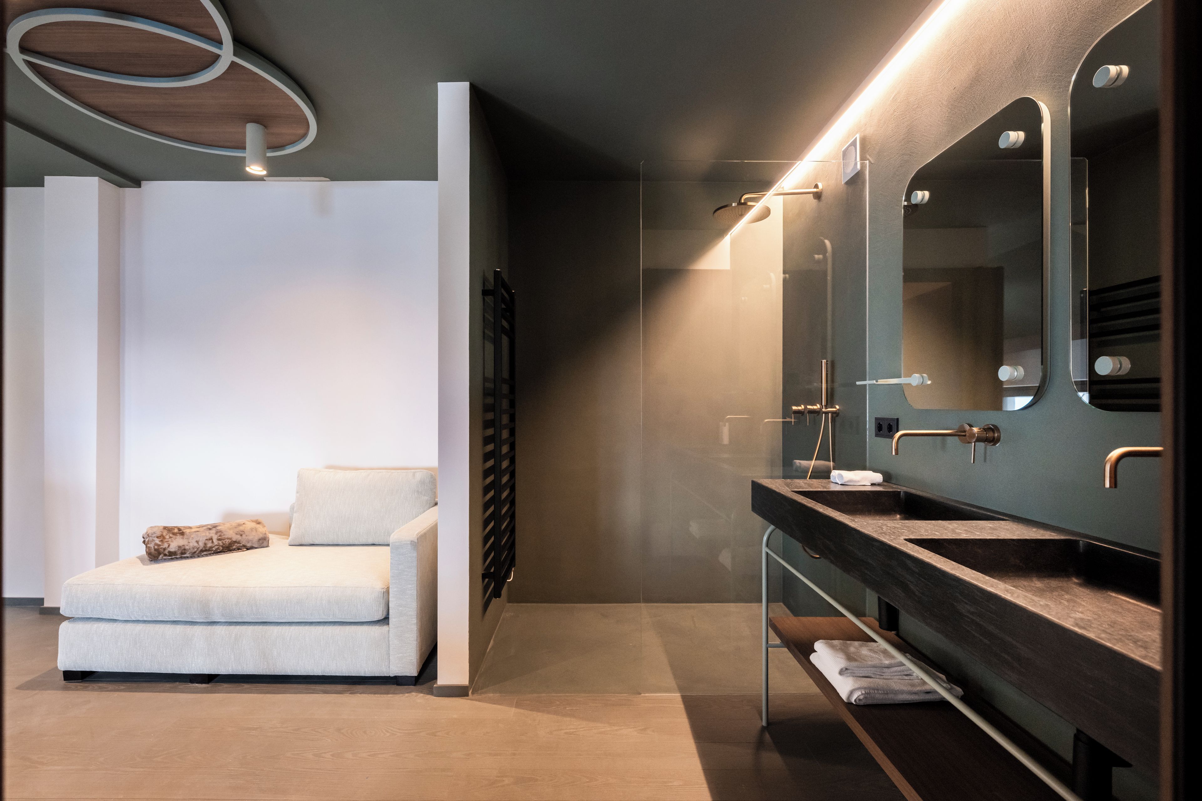 Ein modernes Badezimmer mit einem großen Spiegel, zwei Waschbecken und einer Sitzecke mit Kissen.
