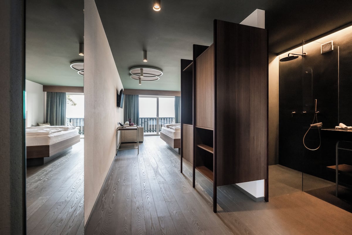 Un baño moderno con ducha, lavabo e inodoro. El suelo es de madera y se aprecia una ventana grande al fondo.