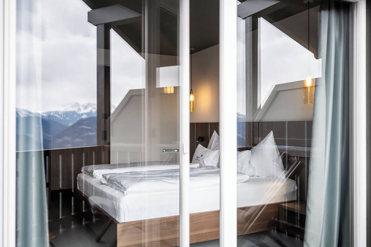 Habitación de hotel moderna con una cama grande, cabecera de madera y vistas a las montañas a través de la ventana.