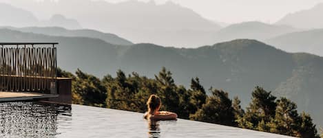 A person relaxing in a clear infinity pool with a view of distant mountains.