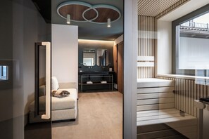 Une chambre d’hôtel moderne équipée d’un canapé, d’un miroir, d’une coiffeuse avec un lavabo et d’un escalier avec une rampe.