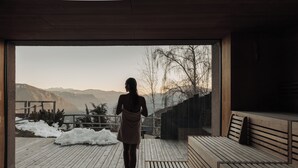 Una persona caminando hacia una terraza de madera con bancos, con vista a un paisaje nevado y montañas.