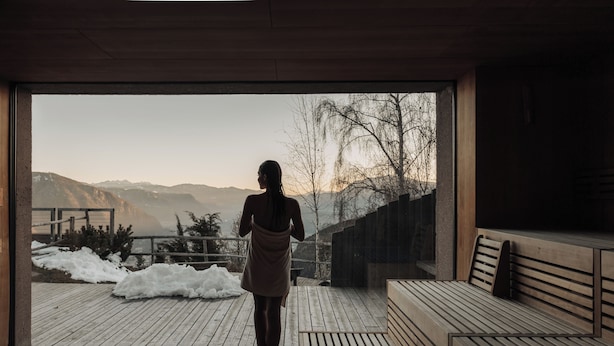 A person walking towards a wooden deck with benches, overlooking a snowy landscape and mountains. - Hotel Belvedere- Fine Dining & SPA (San Genesio Atesino)