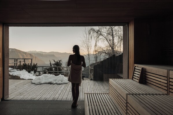 Una persona caminando hacia una terraza de madera con bancos, con vista a un paisaje nevado y montañas.