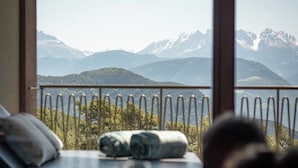 A room with a bed, a window with a view of mountains, and a railing. - Hotel Belvedere- Fine Dining & SPA (San Genesio Atesino)