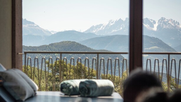 Una habitación con cama, ventana con vista a las montañas y una barandilla.