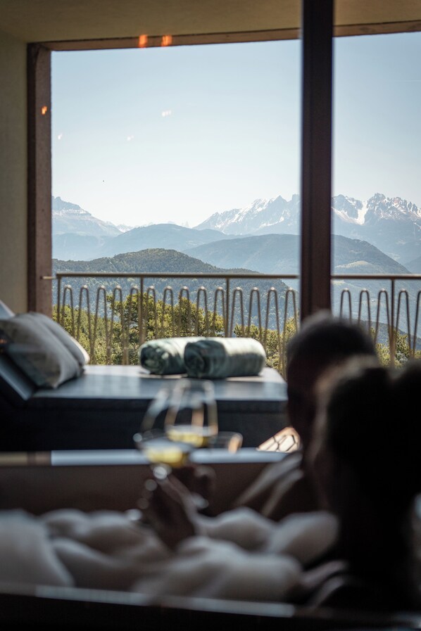 A room with a bed, a window with a view of mountains, and a railing. - Hotel Belvedere- Fine Dining & SPA (San Genesio Atesino)