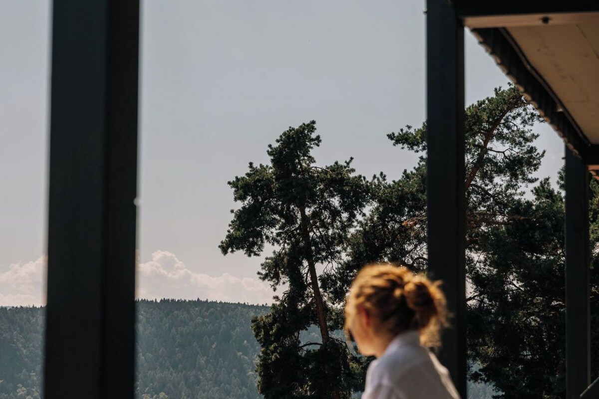 Iemand zit op een balkon met uitzicht op een bebost landschap.