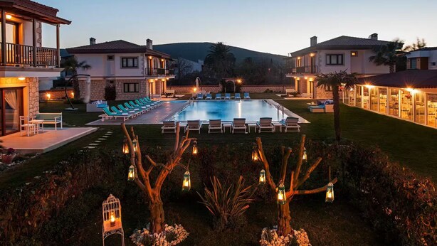 A poolside area with lounge chairs and a swimming pool, surrounded by well-maintained lawns and decorative lighting. - Mara Bahçe Alaçatı (Cesme)