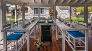 An outdoor dining area with white wooden tables and blue cushioned benches, a chalkboard sign, and stone walls. - Mara Bahçe Alaçatı (Cesme)