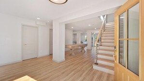 A spacious interior with a wooden floor, a staircase, and a large wooden door.
