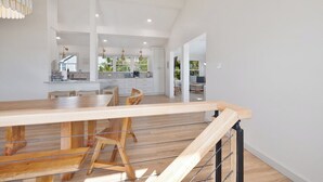 A spacious kitchen with white cabinets, a wooden dining table, and a staircase leading to an upper level.