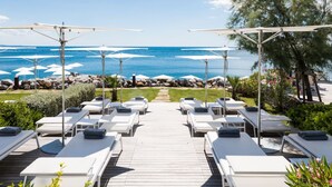 A deck with sun loungers and umbrellas overlooking a beach. - Sea-view Penthouse Spa in Portopiccolo (Duino-Aurisina)