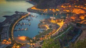 Una località costiera al crepuscolo, con un porto turistico, edifici sul lungomare e un hotel di rilievo con un viale a cerchio.