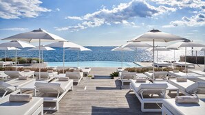 A wooden deck with white lounge chairs and umbrellas overlooking a pool and the sea. - Sea-view Penthouse Spa in Portopiccolo (Duino-Aurisina)