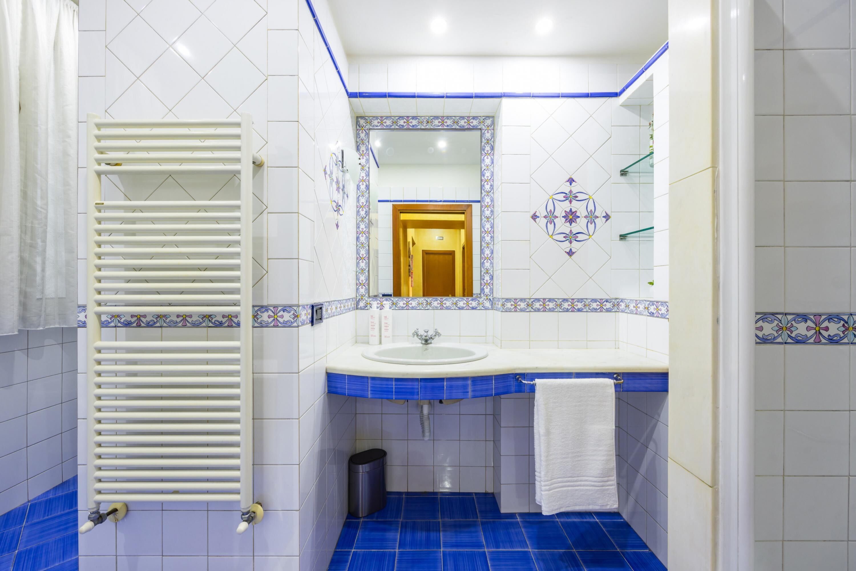 Een badkamer met een wit wastafel, blauwe tegels, een handdoekrek en een spiegel.