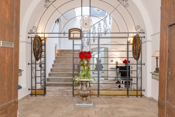 Una imponente entrada con una reja de hierro forjado, una escalera y una urna decorativa con flores rojas.