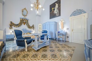 Una habitación con un sillón azul, una mesa blanca, un armario azul y una puerta blanca.