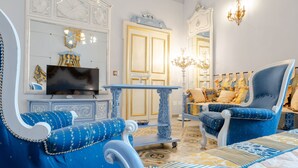 Une chambre avec un grand lit, une télévision, un fauteuil bleu et un lustre.