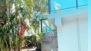 A modern outdoor shower with stone steps and a glass enclosure, surrounded by tropical plants.