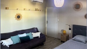 A bedroom with a dark-colored sofa, a bed with a patterned bedspread, a bedside table with a lamp, and decorative wall art.