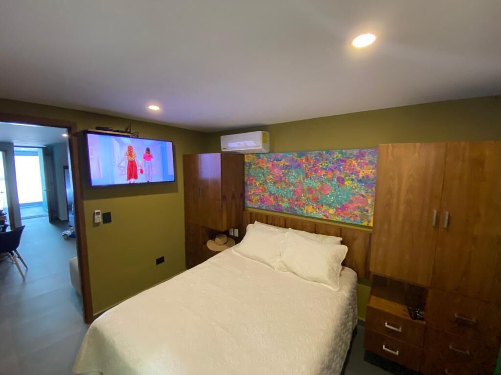 A bedroom with a bed, a television, a colorful abstract painting, and wooden cabinets.