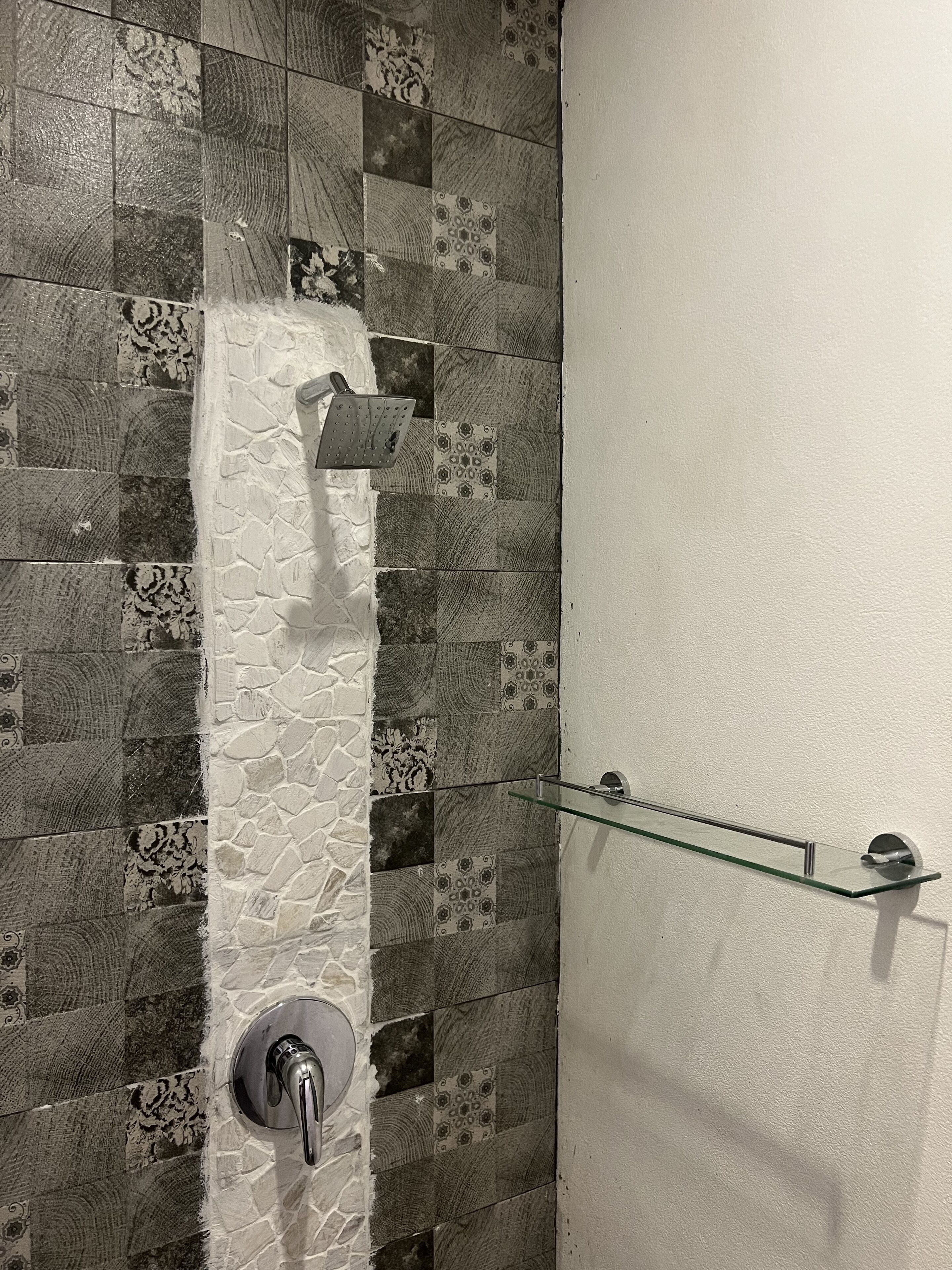 Ducha con pared de piedra y repisa de vidrio.