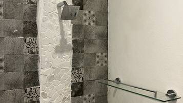 Ducha con pared de piedra y repisa de vidrio.