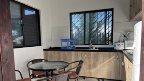 A compact kitchen with a dining area, featuring a round table, chairs, and a small blue rack. - Pasifika Guesthouse (Nadi)