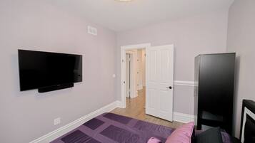 A bedroom with a flat-screen TV mounted on the wall, a bed with a purple quilt, and a black wardrobe.