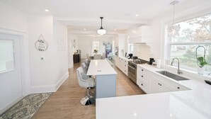 A modern kitchen with a central island, white cabinetry, and a large window providing natural light.
